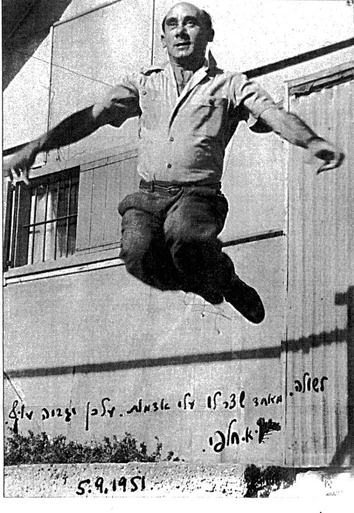 צילום שחור-לבן מ-1951 של אברהם חלפי מנתר באוויר מול מבנה, על התמונה הקדשה בכתב יד
