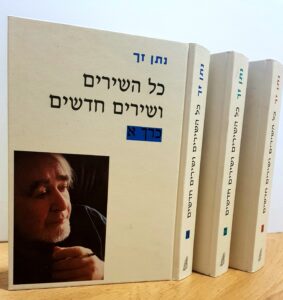 שלושה כרכים של כל השירים ושירים חדשים מאת נתן זך עומדים על מדף, על הכריכה דיוקנו