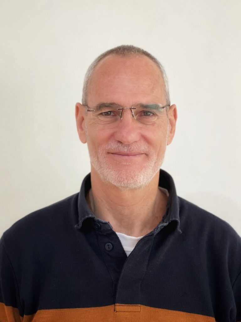 חנן, גבר בשנות החמישים עם משקפיים וחולצה שחורה וכתומה