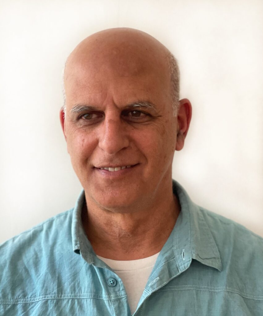 portrait of a man wearing a light blue shirt, smiling at the camera