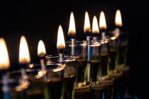 נרות שמן דולקים בכוסיות זכוכית בחנוכייה, בתקריב על רקע שחור