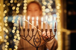 אשה מדליקה נרות בחנוכייה מעוטרת מגן דוד, על רקע אורות מטושטשים
