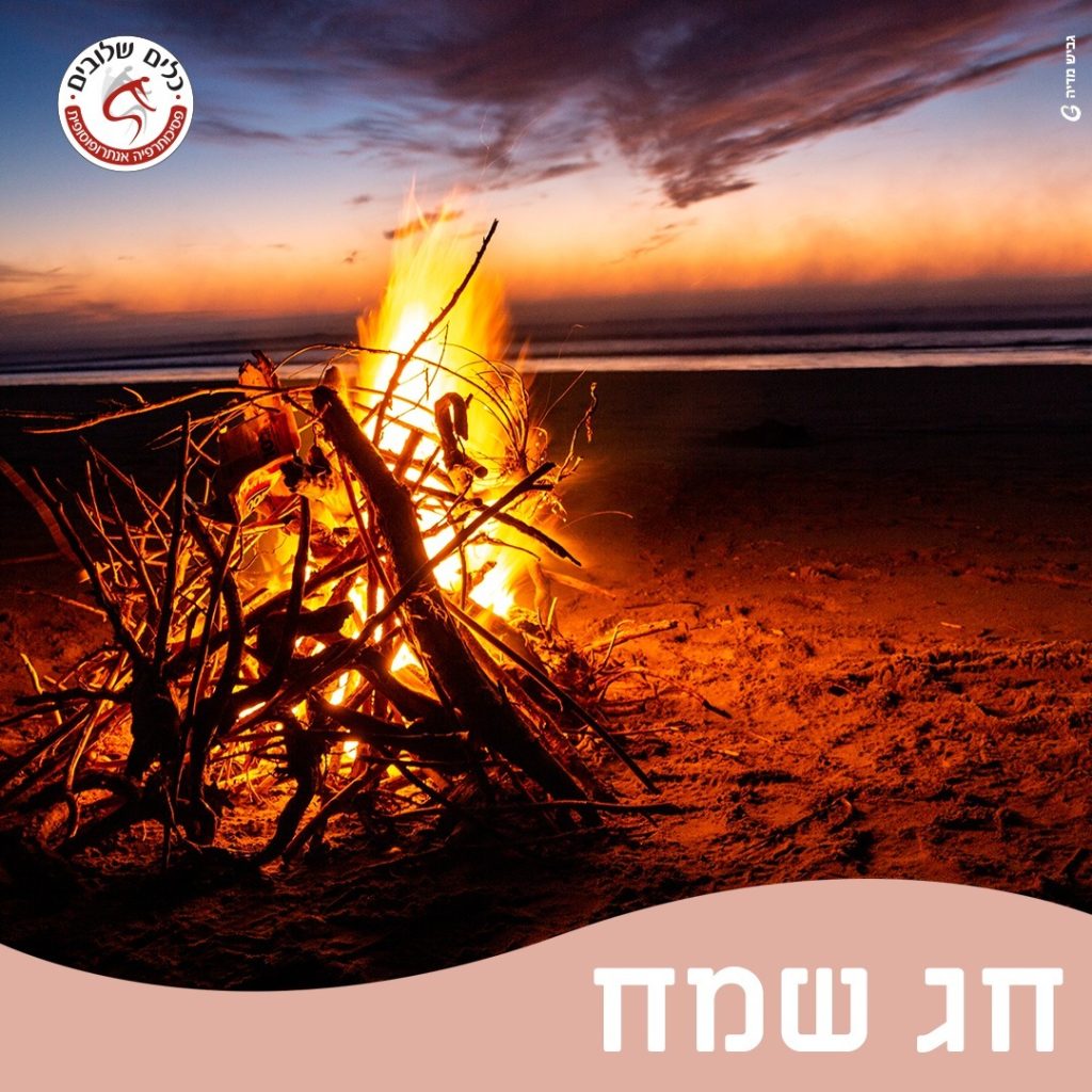מדורה בוערת על חוף הים בשעת דמדומים, לצד הכיתוב חג שמח