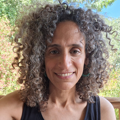דיוקנה של קרן משולם מחייכת, עם שיער מתולתל על רקע צמחייה